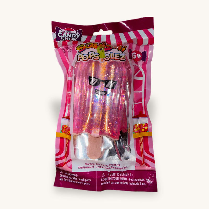 Pink glitter popsicle squishy sealed in its Squishi Popsiclez hanging pack on a wooden table