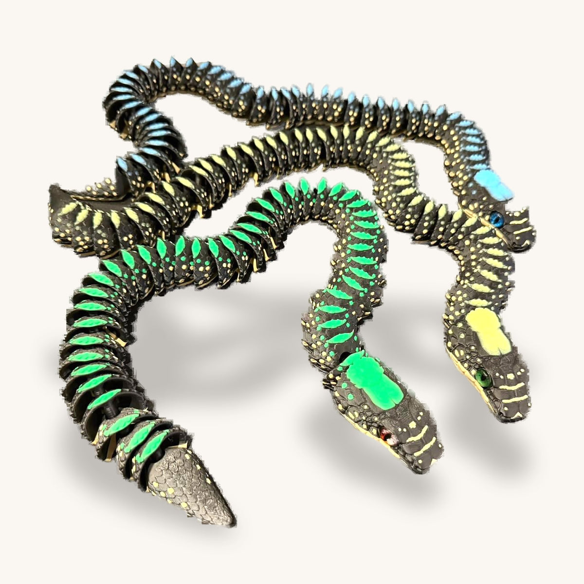 Three 3D-printed articulated snakes, black bodies speckled green and blue, coiled on a plain background
