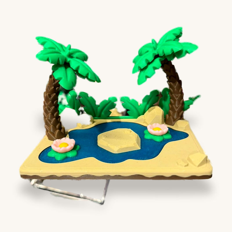 3D-printed miniature scene with two palm trees and a blue pond with water lilies on a sand base