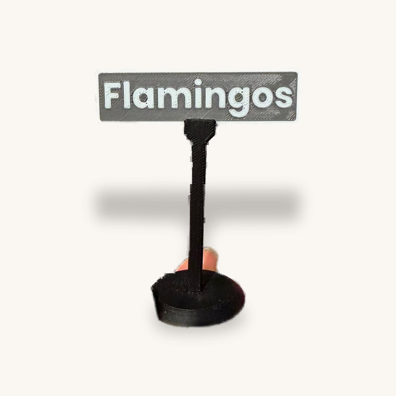 3D-printed miniature sign on a round weighted base reading Flamingos