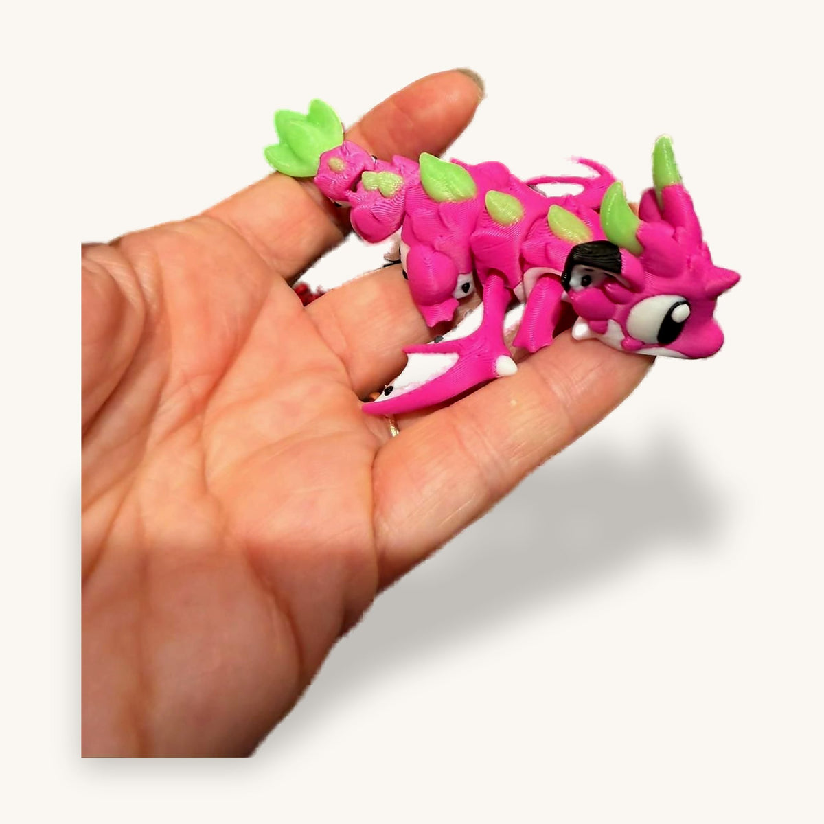 Pink and green 3D-printed articulated baby dragon held in a hand