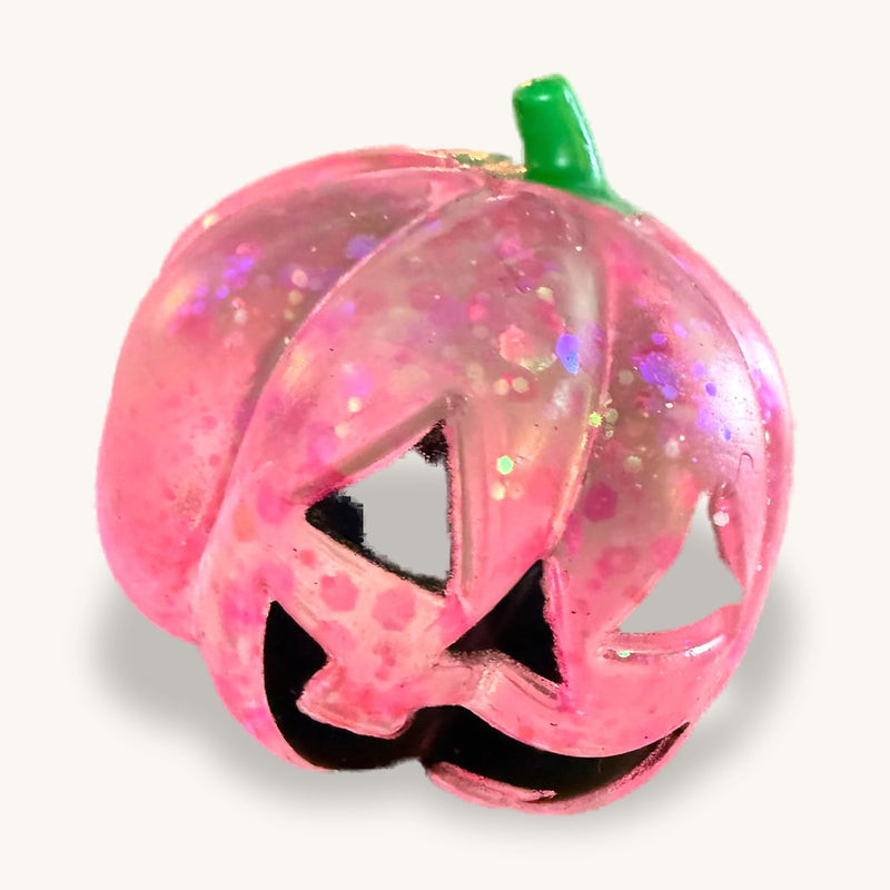 Pink glitter jack-o-lantern squishy on a wooden table, green stem, carved triangle eyes